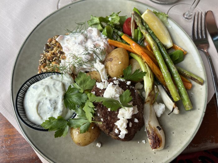 En tallrik med grönsaker, potatis, biff, tzatziki, sallad och bröd. Färgrik, aptitretande och portionerad måltid.