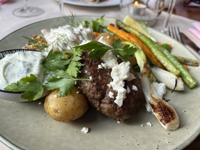 En tallrik med köttbiff, potatis, grillade grönsaker, tzatziki och färsk persilja.