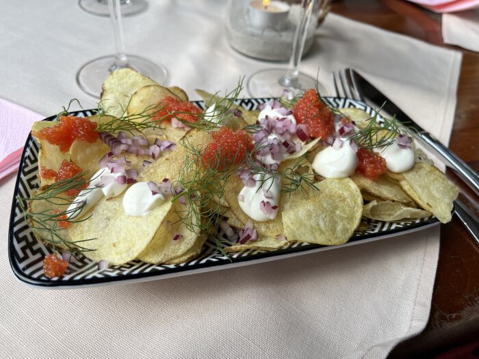 Chips med löjrom, crème fraîche, rödlök, dill. Serveras på restaurang, sofistikerad presentation, aptitretande.