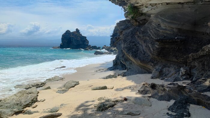 Klippig strand, turkos hav, klar himmel, stenformationer, sandstrand, och vågor. Naturskön exotisk plats.