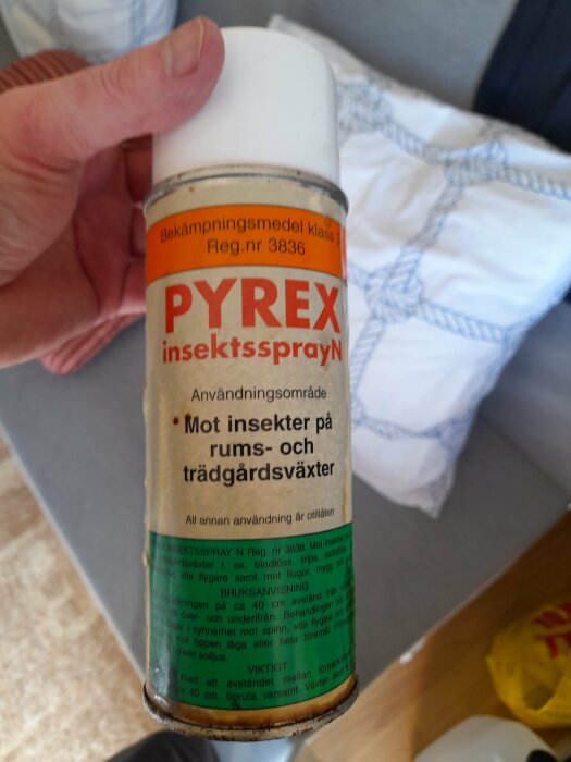 En hand håller en gammal Pyrex insektssprayflaska mot en inomhusbakgrund.