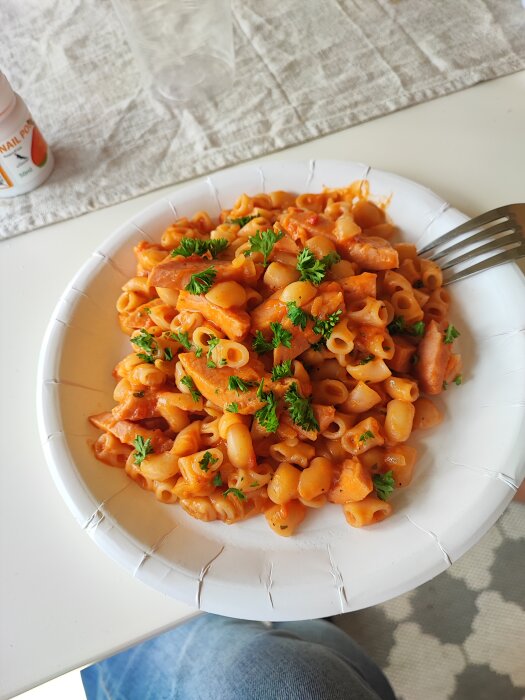 Tallrik med pasta och tomatsås, garnerad med persilja, på ett bord med linneduk.