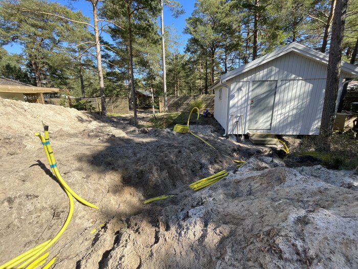 Grävplats med gula rör, vit byggnad, träd, skuggor och soligt.