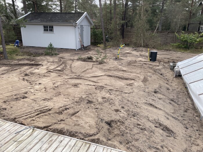 Trädgårdsområde under ombyggnad eller anläggning med sand, skjul, leksaker och byggmaterial synliga.