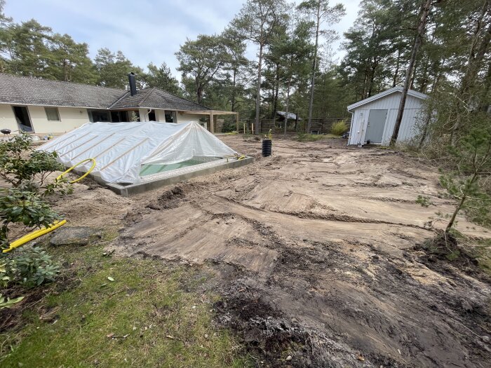 Husbygge eller renovering, grunden täckt med presenning, skogsmiljö, byggnadsarbetsplats med utspridd jord och utrustning.