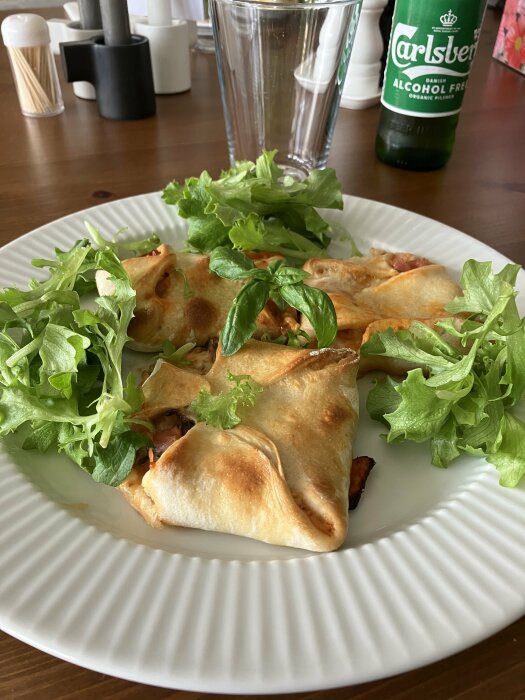 Serverade samosas med sallad, basilika, alkoholfri öl, transparent glas och kryddkvarnar på träbord.