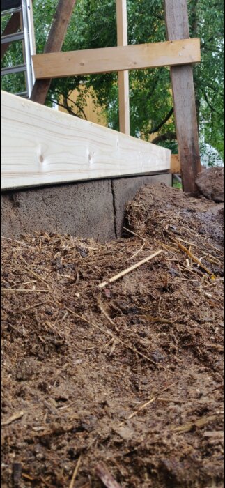 Byggarbetsplats med stege, nytt trä, murblock och hög med organiskt material. Utomhus, dagtid, eventuellt trädgårdsprojekt.