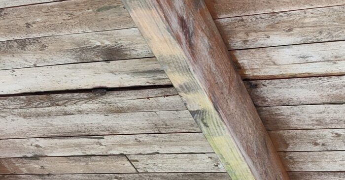 Trägolv och en lutande trästång med strukturerade mönster och ådringar. Naturlig, sliten yta med skruv.