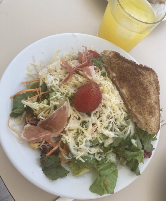 Färgglad sallad med ost, prosciutto, jordgubbe och macka, juiceglas, ljus bakgrund.