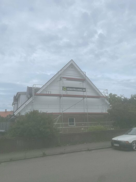 Hus i ställningar, möjlig renovering, bil framför, dimmig himmel, grönska, bostadsområde.