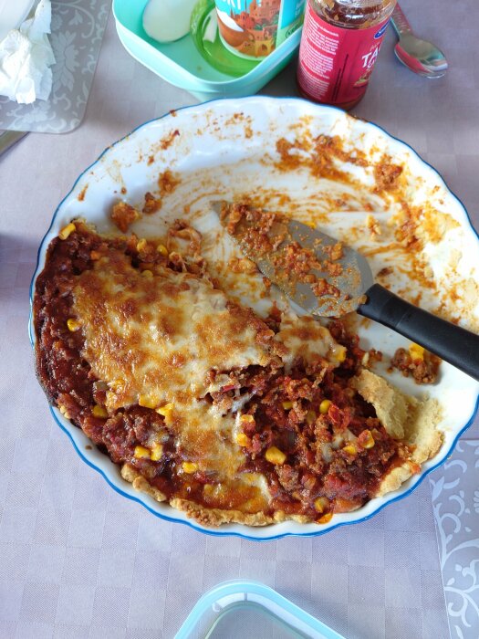 Halväten lasagne i form, tomatsås, ost, köttfärs, majs, serveringsspad i bakgrunden, matbordsduk.