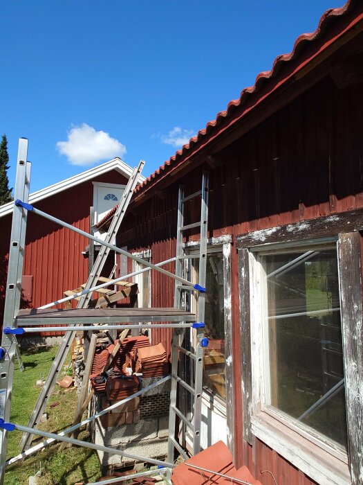 Husfasad under renovering, stege, byggnadsställning, tegeltakpannor, soligt, blå himmel, gammalt fönster.