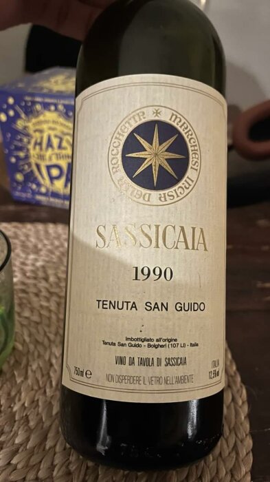 Flaska Sassicaia vin, 1990, Tenuta San Guido, etikett, kompass-stjärna, bakgrund med person och förpackning.