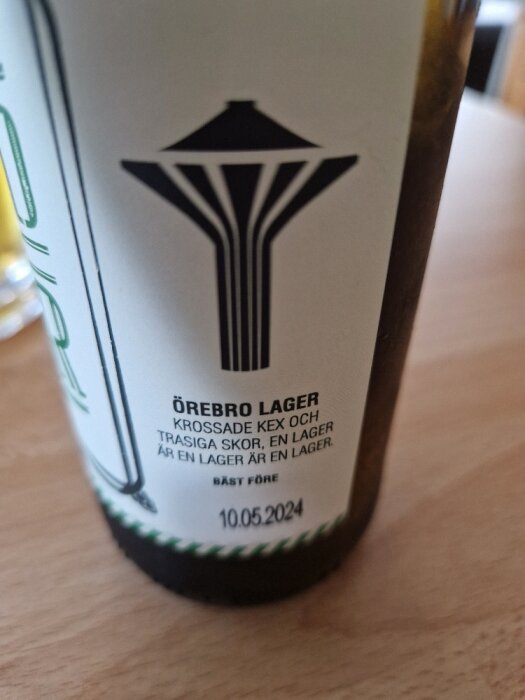 Ölflaska med etikett, "Örebro Lager", bäst-föredatum, svartvita grafiska element, text på svenska.