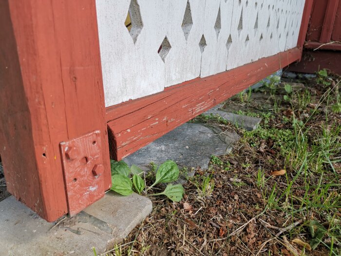 Röd stolpe, vit vägg med dekorativa utskärningar, försummad trädgård, slitna färger, stentrappa.