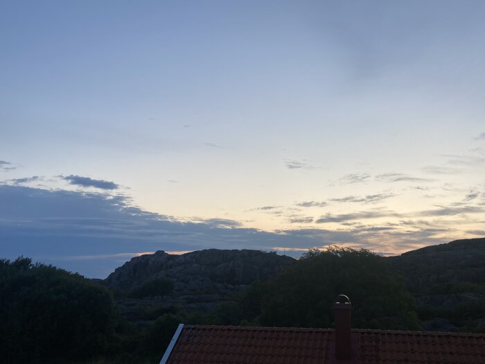 Skymning, moln, solnedgångsglöd på klippor, röda hustak, lugn, natur och bostad kombinerat.