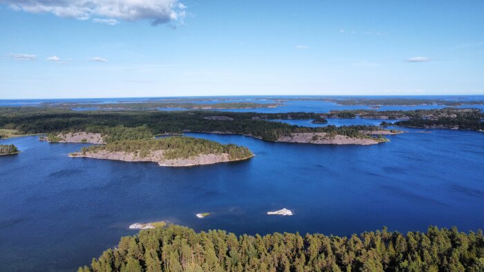 Flygbild av skärgård med blått vatten, gröna öar och skog. Klart väder med några moln.