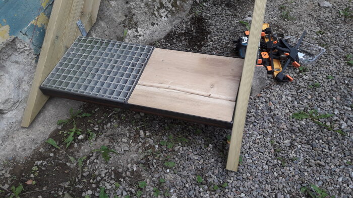 Gör-det-själv trädgårdsprojekt, träbänk under konstruktion, verktyg och klämmor på grus.