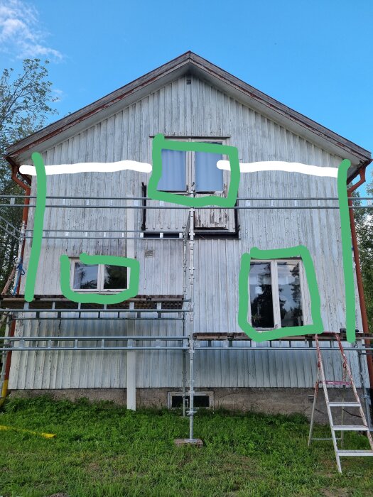 Ett hus med byggnadsställningar och oavslutad målningsarbete på fasaden; fönster ej målade, omgivna av grönt landskap.