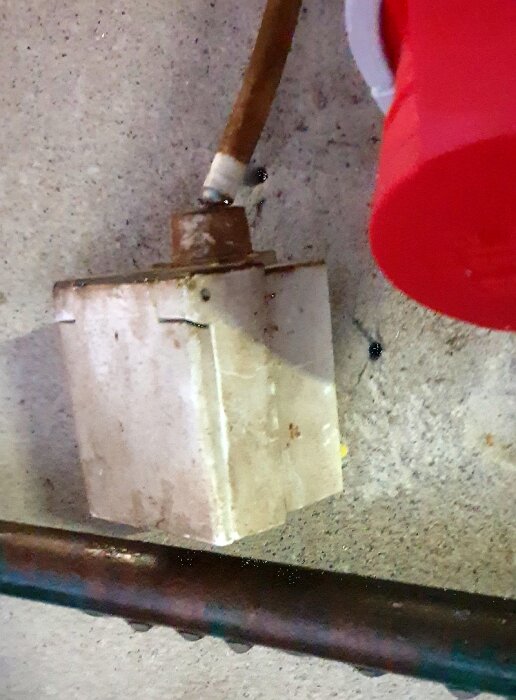 En rostig, upphängd box med kablar intill en röd detalj, troligen industriell eller mekanisk installation.