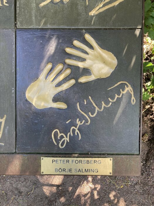 Avtryck av händer och signatur i relief på platta, namnskylt nedanför med Peter Forsberg och Börje Salming.