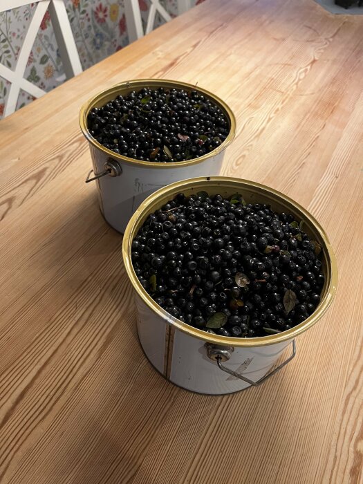 Två hinkar fyllda med blåbär på ett träbord, blad bland bären, lantligt kök.