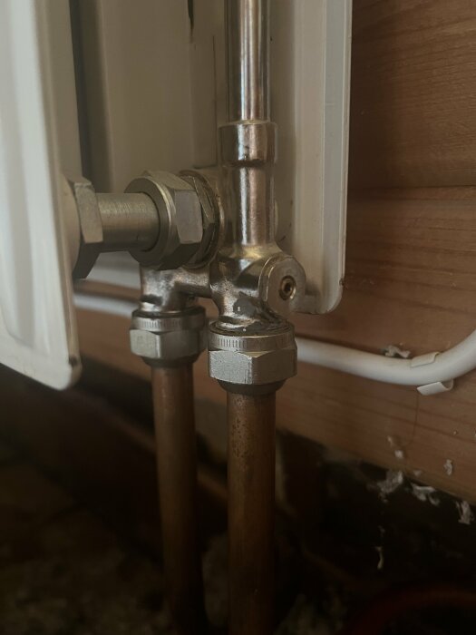 Rörledningar och ventiler vid vägg, potentiellt för uppvärmning eller vatten, med tecken på åldring eller slitage.