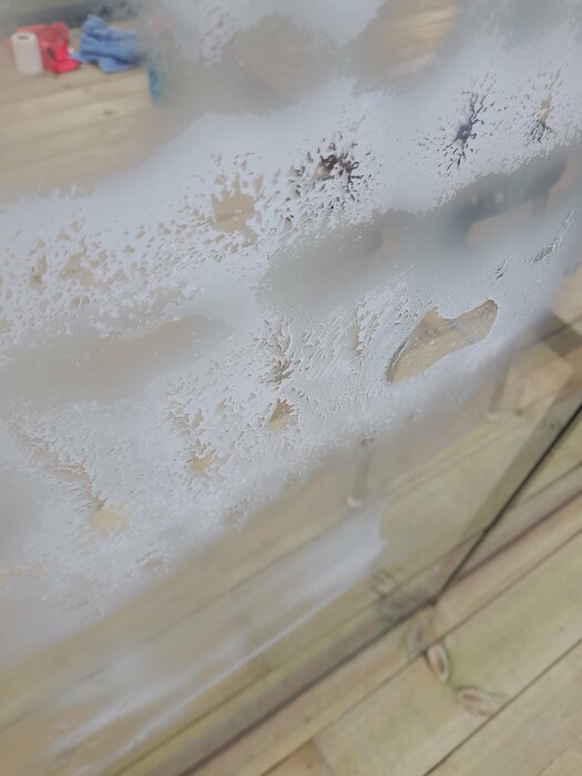 Isfron på fönster, suddig bakgrund med trägolv och hushållsartiklar. Frostigt mönster, vinterkyla eller dålig isolering.