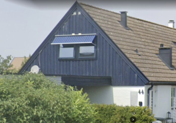 Ett blått hus med snedtak, vita knutar, fönster, och en parabolantenn.
