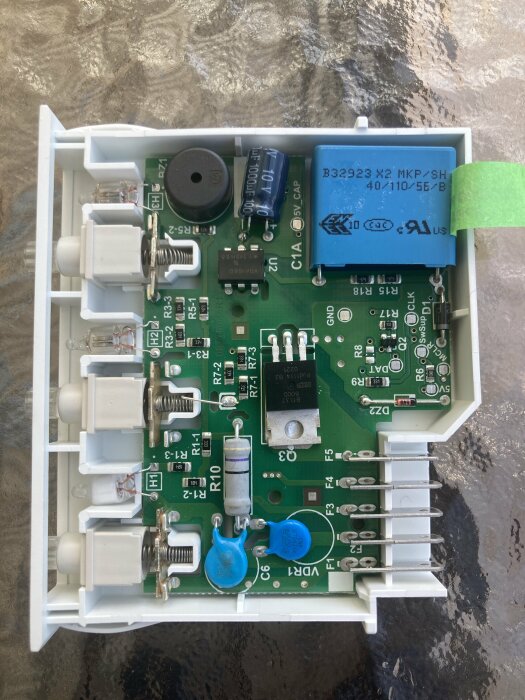 Elektronikkort inuti vit plasthölje med kondensatorer, relä, transistorer och anslutningsterminaler.