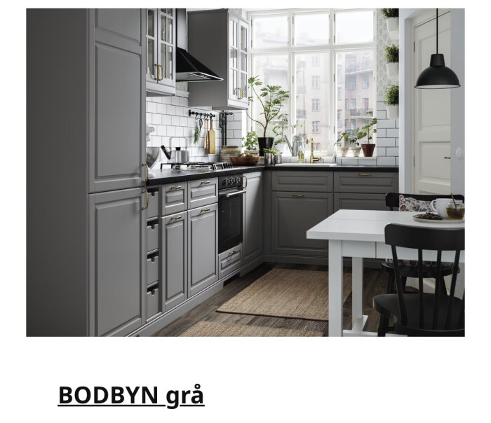 Modernt kök med grå skåp, vita kakelväggar, fönster, matbord, stolar och gröna växter.