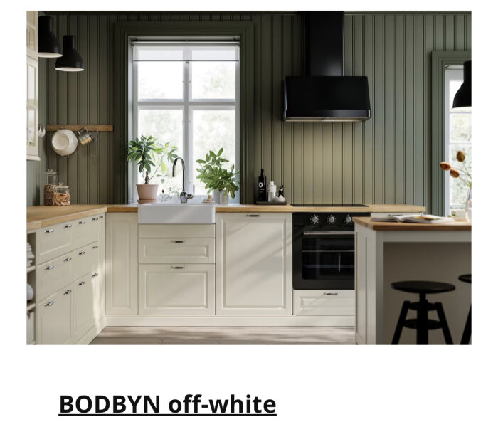 Modernt kök med off-white skåp, träbänkskivor, svarta detaljer, gröna växter, fönster och inbyggd ugn.