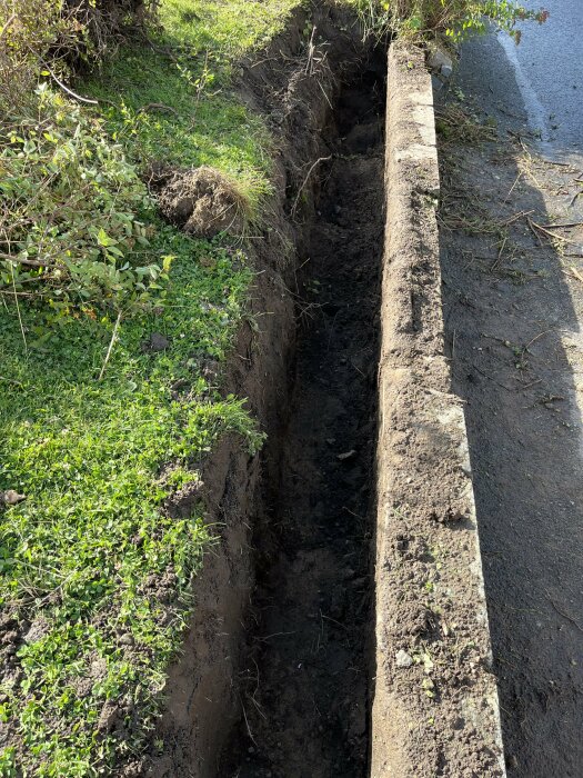 Erosion eller grävning vid vägkant skapat djupt dike; grönt gräs och jord syns.