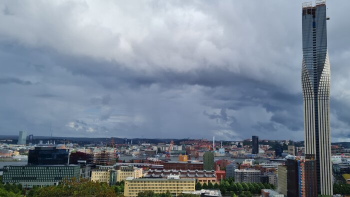 Stadssilhuett, skyskrapa, molnig himmel, bebyggelse, dramatiskt väder, dagtid, stadsvyer, kranar, arkitektur.