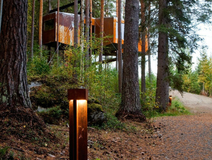 En trädkoja med modern design i en skog nära en stig med en belyst vägmarkering.