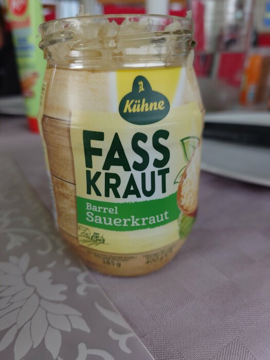 Öppnad burk med sauerkraut på ett duk, märket Kühne, i förgrunden. Bakgrunden är suddig.