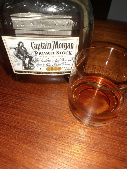 En Captain Morgan romflaska och ett glas med rom på ett träbord.