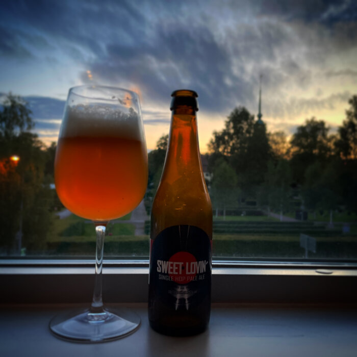 Ölglas på fönsterbräda, flaska, skymning, träd, molnigt himmel, inomhusutsikt, avkoppling, "Sweet Lovin'" etikett.