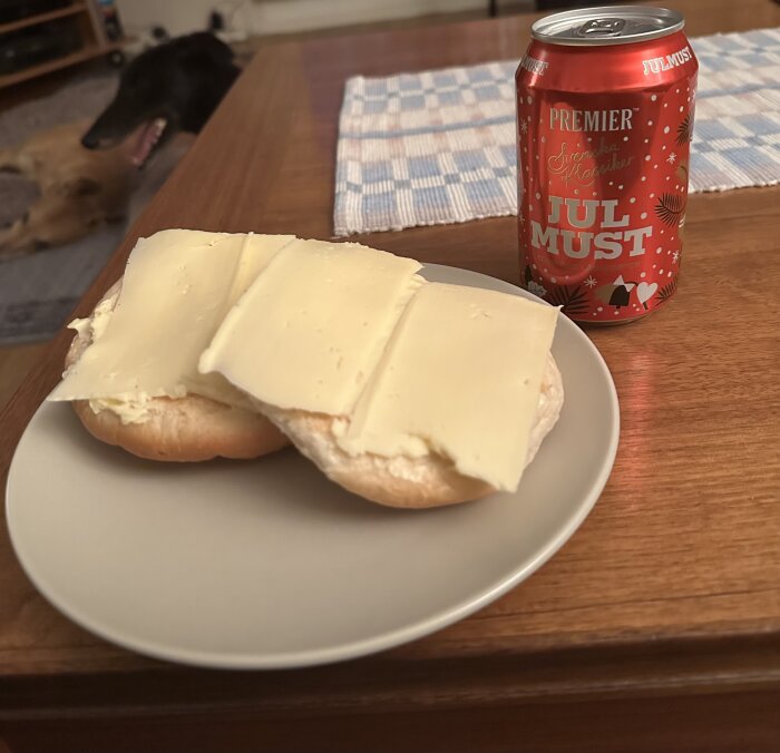 Bulle med ost på tallrik, julmust på burk, bakgrunden visar en hund och ett köksbord.