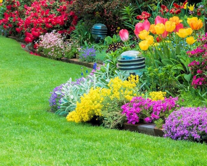 Välskött trädgård med frodig grönska, färgglada blommor, prydligt klippt gräsmatta och dekorativa trädgårdsklot.