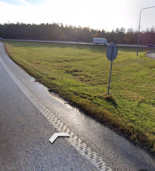 Landsväg med avfartsramp, markeringsskylt, gräs, lastbil i rörelse, träd, solnedgång.