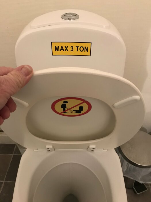 En toalettstol med rolig skylt "MAX 3 TON" och en symbol som förbjuder hukande position.