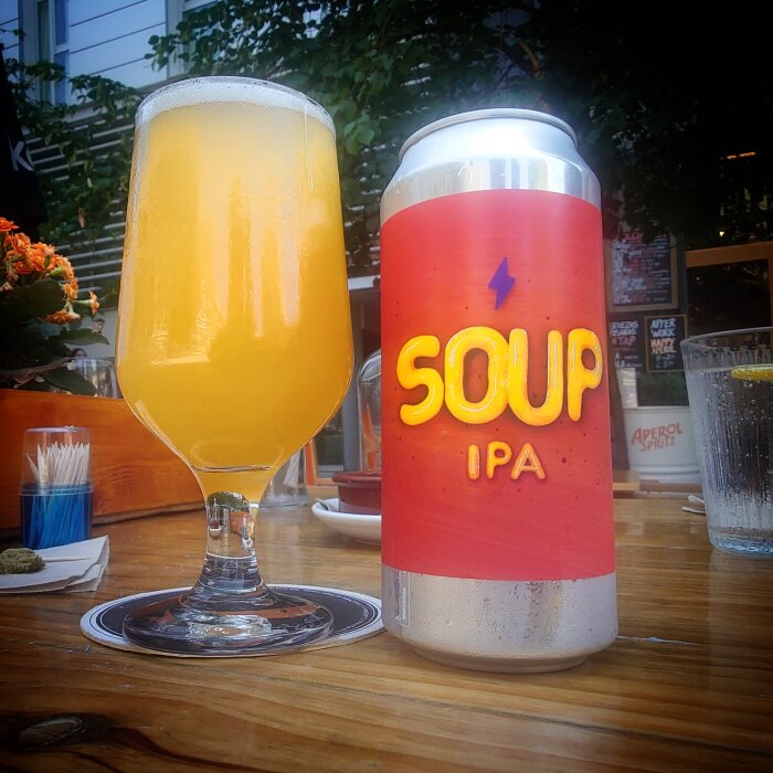 Ölglas med grumlig IPA bredvid en burk märkt "SOUP IPA" på ett utebord.