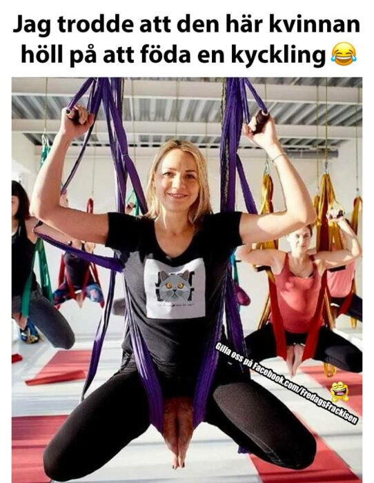 Kvinna ler, yogar med lila hängmatta, humoristisk bildtext om kyckling, andra deltagare i bakgrunden.