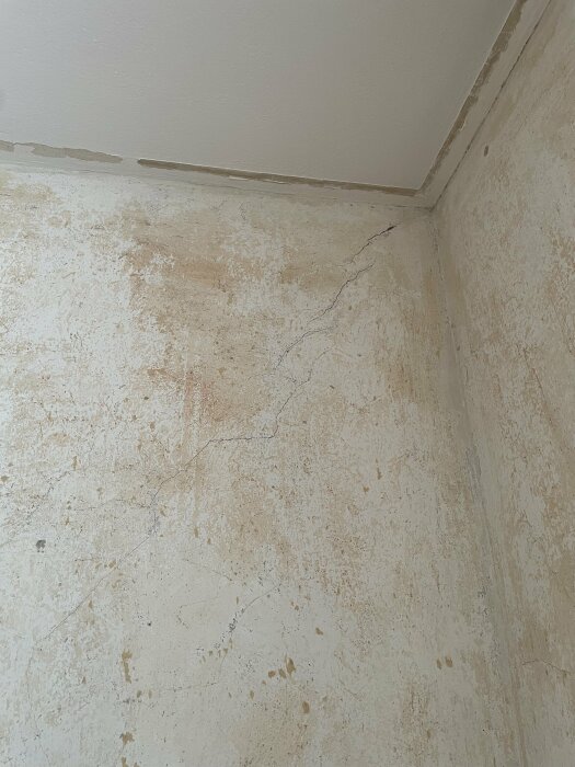 Hörn av ett rum med sprickor och fuktskador på vägg och tak.