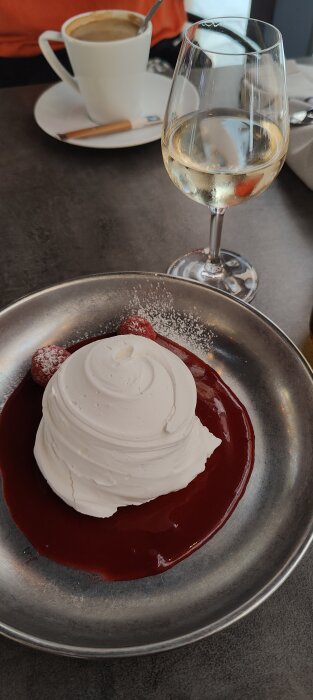 Dessert med maräng och bär i röd sås, kaffekopp och glas med vitvin. Eleganta serveringsfat, del av måltid.