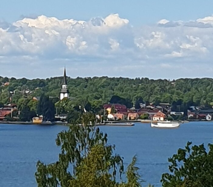 Kuststad, kyrka, båtar, träd, moln, lugnt vatten, ljusreflektioner, sommar, pittoreskt, skandinaviskt landskap.