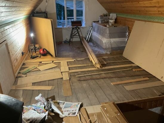 Oavslutat golvprojekt i rum med lutande tak, byggmaterial och verktyg utspridda, renoveringsarbete pågår.