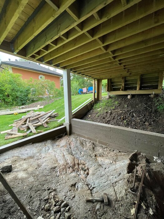 trädäck under konstruktion, trädgårdsutsikt, virkesavfall, grå dag, renoveringsprojekt, obehandlat trä, gräs, grävmaskin, verktyg.