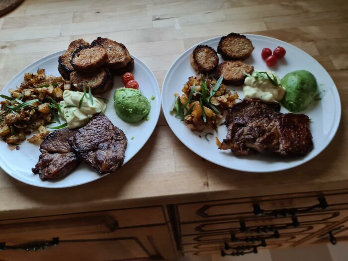 Två tallrikar med stek, potatis, bröd, sås och grönsaker på ett träbord.